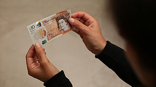 A KINEGRAM COLORS® Stripe over Window is the principal security feature on the English Pound banknotes 2 hands holding an English 10 Pound banknote with a security feature by KURZ