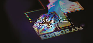 Close-up of a KINEGRAM® security feature showing guilloche shaped fine lines and a Swiss Cross in 3D